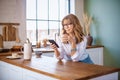 Smiling woman text messaging and drinking morning coffee while standing in the kitchen at home Royalty Free Stock Photo