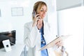 Smiling female doctor using her mobile phone while reviewing some papers in the consultation Royalty Free Stock Photo