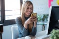 Smiling young business woman using her mobile phone while working with computer in the office Royalty Free Stock Photo