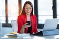 Smiling young businesswoman using her mobile phone while working with computer in the office Royalty Free Stock Photo