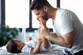 Smiling young father has fun with little baby while changing his nappy at home