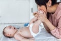 Smiling young mother has fun with little baby while changing his nappy at home