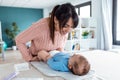 Smiling young mother has fun with little baby while changing his nappy at home