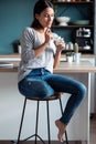 Smiling young woman eating yogurt while sitting on stool in the kitchen at home Royalty Free Stock Photo