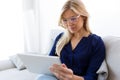 Smiling young woman using her digital tablet while sitting on sofa at home.