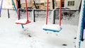 Closeup shot of snow covered playground. Two swings under snow in the park