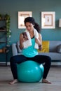 Sporty african young woman using her mobile phone after session of exercises while sitting on fitness ball at home Royalty Free Stock Photo