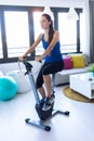 Sporty young woman exercising on smart stationary bike and listening to music at home Royalty Free Stock Photo