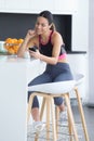 Sporty young woman listening to music with mobile phone while eating yogurt in the kitchen at home Royalty Free Stock Photo