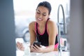 Sporty young woman listening to music with mobile phone while eating yogurt in the kitchen at home Royalty Free Stock Photo