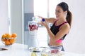 Sporty young woman preparing strawberry and banana smoothie with blender in the kitchen at home