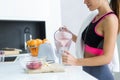 Sporty young woman serving strawberry smoothie in a glass jar in the kitchen at home