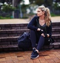 Getting psyched before her workout. Shot of a sporty young woman sitting outside with a gym bag.