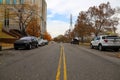 A shot of a street with a yellow line in the center with parked cars along the street and gorgeous autumn colored trees