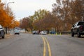 A shot of a street with a yellow line in the center with parked cars along the street and gorgeous autumn colored trees