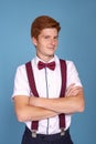 Shot of a  stylish red-haired young smiling boy teenager wearing  white shirt with a red bow tie and suspenders  with arms crossed Royalty Free Stock Photo