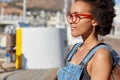 Shot of stylish teenage girl with Afro haircut, wears optical glasses for good vision, dressed in denim overalls Royalty Free Stock Photo