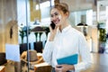 Stylish young businesswoman talking with her mobile phone while holding her digital tablet standing in the hotel lobby Royalty Free Stock Photo