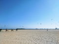 A shot of a sunny day at the beach with people flying kites and blue sky