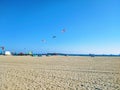 A shot of a sunny day at the beach with people flying kites and blue sky