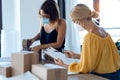 Two beautiful freelance business women seller wearing a hygienic facial mask while checking product order while packing and Royalty Free Stock Photo