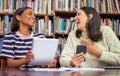 Make each day a little better than before. Shot of two females using their devices in a library. Royalty Free Stock Photo