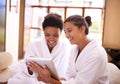 Checking in At the spa. Shot of two friends in bathrobes using a digital tablet at a spa. Royalty Free Stock Photo