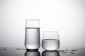 Shot of two glass of water - highball glass and whiskey glass on the white surface with shadows