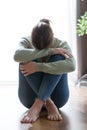 Unhappy lonely and depressed young woman hiding her face between legs at home.