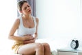 Unhealthy young woman with stomachache leaning on the couch at home.