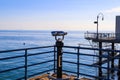 A shot of the vast blue ocean water and beach from the pier with a telescope and blue railing on the pier with blue sky Royalty Free Stock Photo