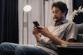 Shot view of man reads online book on smart phone and sitting on soft couch against bright lamp Royalty Free Stock Photo