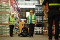 Shot of warehouse workers are pulling a pallet truck walking through rows of tall shelves full of packed boxes. Logistic Royalty Free Stock Photo