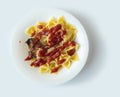 Shot on a white background. No isolation. White plate in it pasta and a piece of meat and a fork