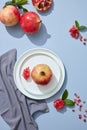 Shot of white plates of whole and sliced pomegranates, leaves and linen napkins on blue table