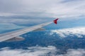 A shot through a window of an airplane shows the wings and the view below, with a number of clouds partially obscuring the view