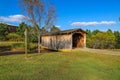 A shot of a wooden covered bridge over a river surrounded by lush green and autumn colored trees with lush green grass Royalty Free Stock Photo