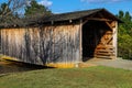 A shot of a wooden covered bridge over a river surrounded by lush green and autumn colored trees with lush green grass Royalty Free Stock Photo