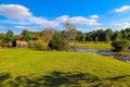 A shot of a wooden covered bridge over a river surrounded by lush green and autumn colored trees with lush green grass Royalty Free Stock Photo