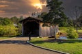 A shot of a wooden covered bridge over a river surrounded by lush green and autumn colored trees with lush green grass Royalty Free Stock Photo