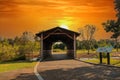 A shot of a wooden covered bridge over a river surrounded by lush green and autumn colored trees with lush green grass Royalty Free Stock Photo