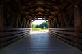 A shot of a wooden covered bridge over a river surrounded by lush green and autumn colored trees with lush green grass Royalty Free Stock Photo