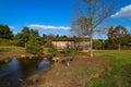 A shot of a wooden covered bridge over a river surrounded by lush green and autumn colored trees with lush green grass Royalty Free Stock Photo