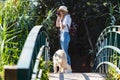 Young amateur photograph woman taking a photo of the landscape while walking with her dog crossing over a bridge in the park Royalty Free Stock Photo