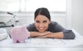 Her company and her savings are growing. Shot of a young architect resting on some blueprints and looking at a piggybank Royalty Free Stock Photo