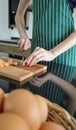 Shot of young Asian woman`s hands slices sausage on wooden plate