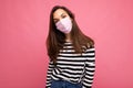 Shot of young attractive bunette woman wearing mediacal face mask isolated over pink background wall. Protection against