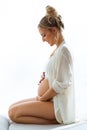 Young beautiful pregnant woman touching and looking her belly sitting on her legs on isolated background Royalty Free Stock Photo