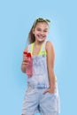 A young brunette girl wearing  denim overalls shorts stands with  a red bottle of water Royalty Free Stock Photo