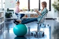 Young business woman using her mobile phone while resting feet on the fitness ball in the office. In the background, her colleague Royalty Free Stock Photo